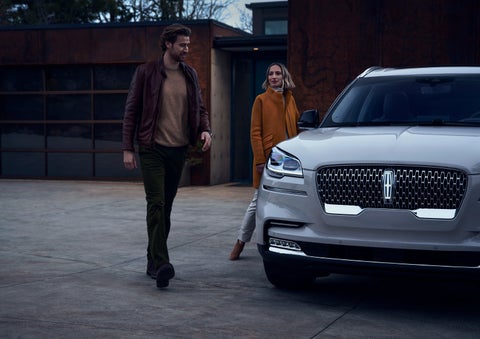 A man and a woman approaching a 2024 Lincoln Aviator® SUV, which illuminates certain lights when they are close | George Ballentine Lincoln in Greenwood SC