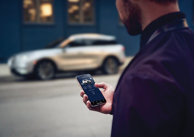 A person is shown interacting with a smartphone to connect to a Lincoln vehicle across the street. | George Ballentine Lincoln in Greenwood SC
